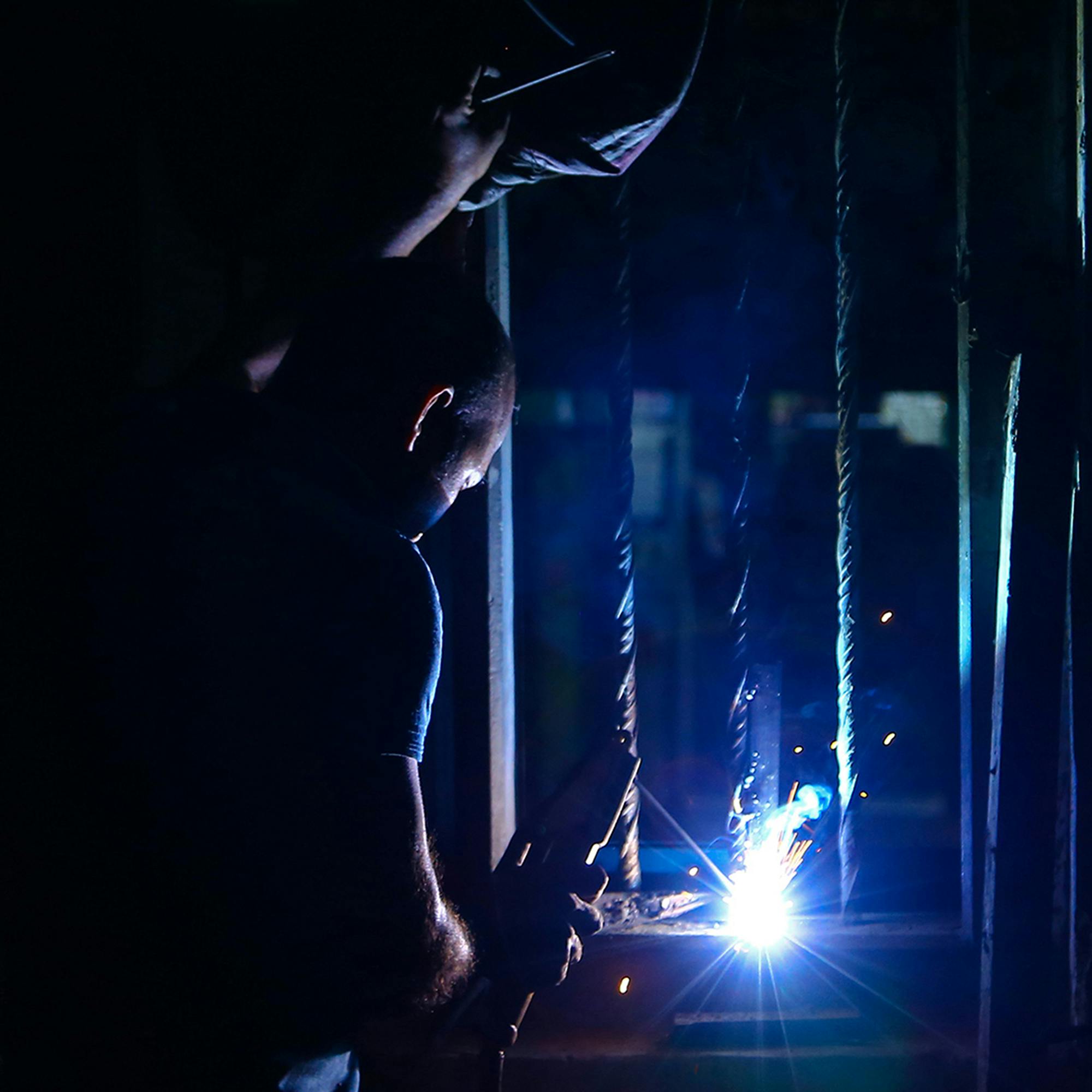 A skilled welder working with bright sparks in a dimly lit industrial environment.